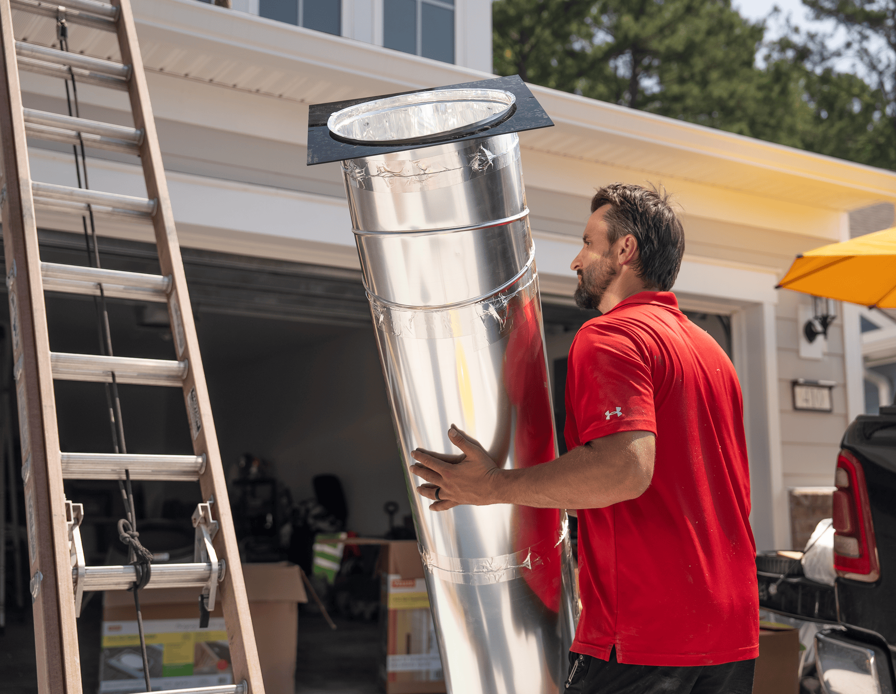 Tubular skylight installer holding tube about to climb a ladder.